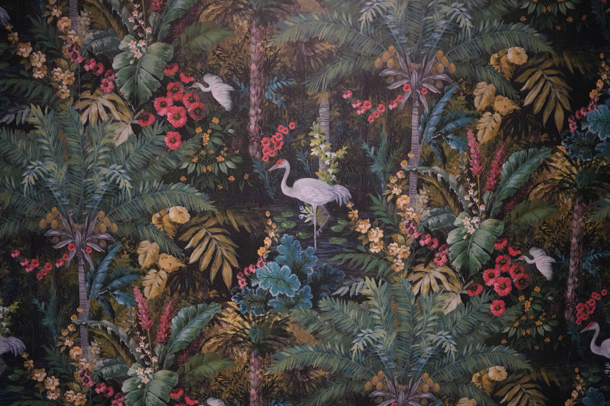 Patterned wallpaper with white cranes standing among tropical plants and colorful flowers in a dense, lush jungle setting.