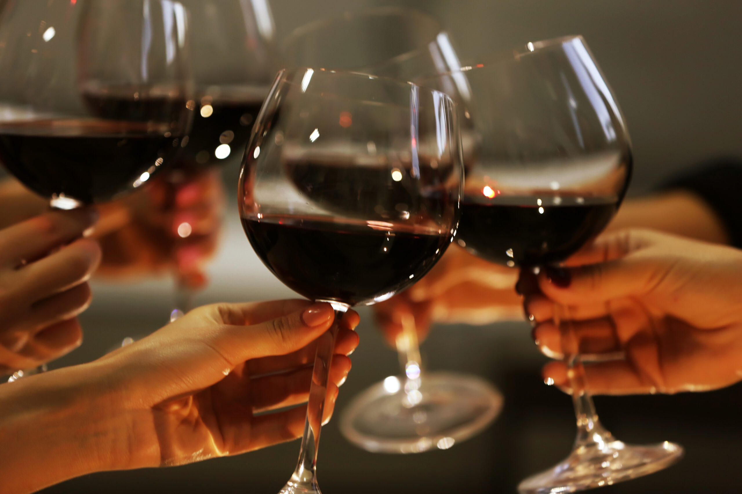 Several hands holding and clinking glasses of red wine in a toast.