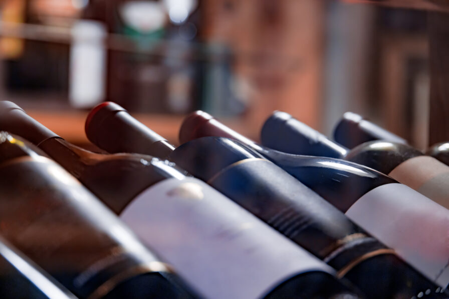 Close-up of several wine bottles lying on their sides in a rack, with labels partially visible and a blurred background.